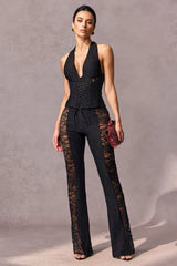 Woman wearing a black lace halter top and flared pants with lace insets