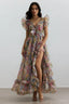 Woman wearing a floral print chiffon gown with V-neck, bow detail, flutter sleeves, and a high-low hemline with a thigh-high slit.