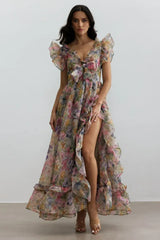 Woman wearing a floral print chiffon gown with V-neck, bow detail, flutter sleeves, and a high-low hemline with a thigh-high slit.