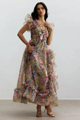 Woman standing in a floral print chiffon gown with V-neck, bow detail, flutter sleeves, and a high-low hemline.