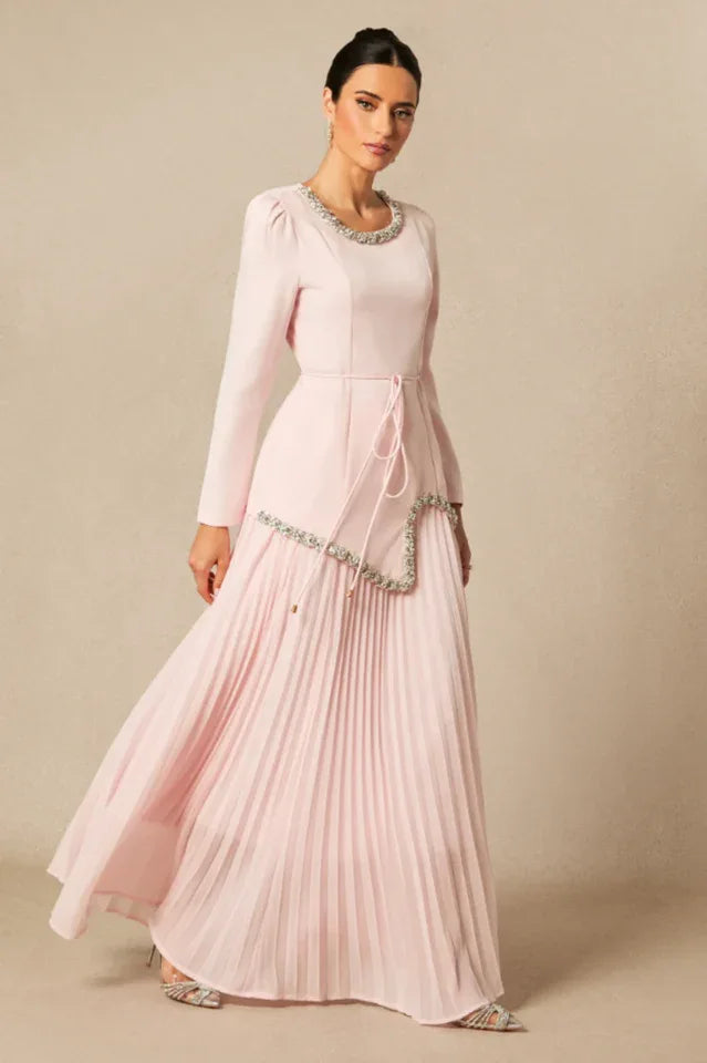 Woman in a light pink, long-sleeved formal dress with a pleated skirt, shown in motion.