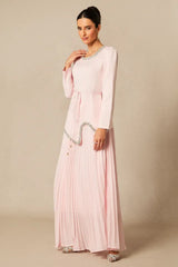 Woman posing in a light pink, long-sleeved formal dress with a pleated skirt and embellished details.