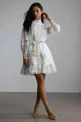 Woman posing in a white floral dress with a high neckline and tiered skirt