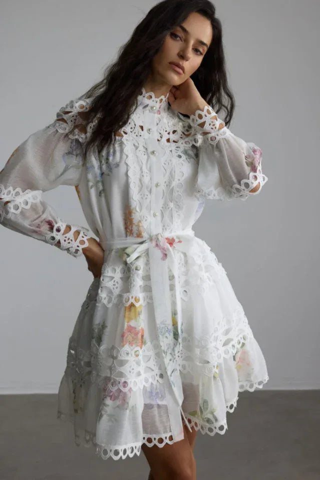 Woman wearing a white floral print mini dress with lace trim and long sleeves