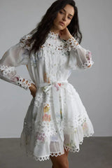 Woman wearing a white floral print mini dress with lace trim and long sleeves