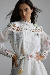 Full-body shot of a woman modeling a white floral print mini dress with a belted waist
