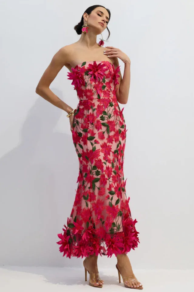 Woman wearing a pink strapless midi dress with floral embellishments and a trumpet skirt, looking to the side.