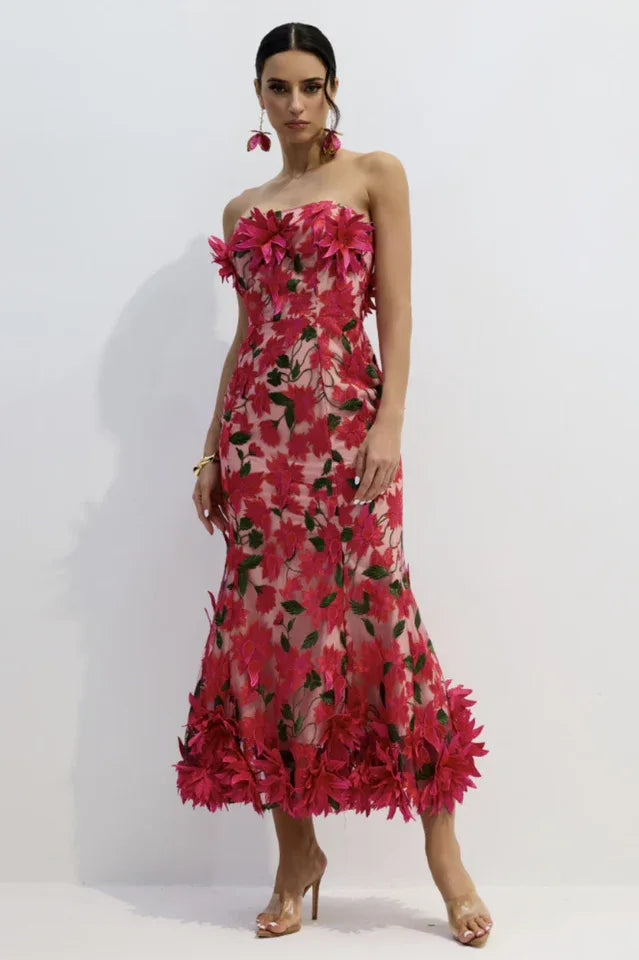Woman wearing a pink strapless midi dress with floral embellishments and a trumpet skirt, posing.