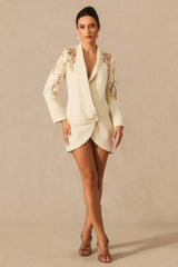 Full-length front view of a woman in a cream tuxedo dress with embellished shoulders.