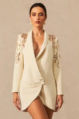 Woman wearing a cream tuxedo dress with embellished shoulders and a deep V-neckline.