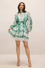 Woman wearing a green and white cut-out mini dress with long puff sleeves and a belted waist, standing and posing.