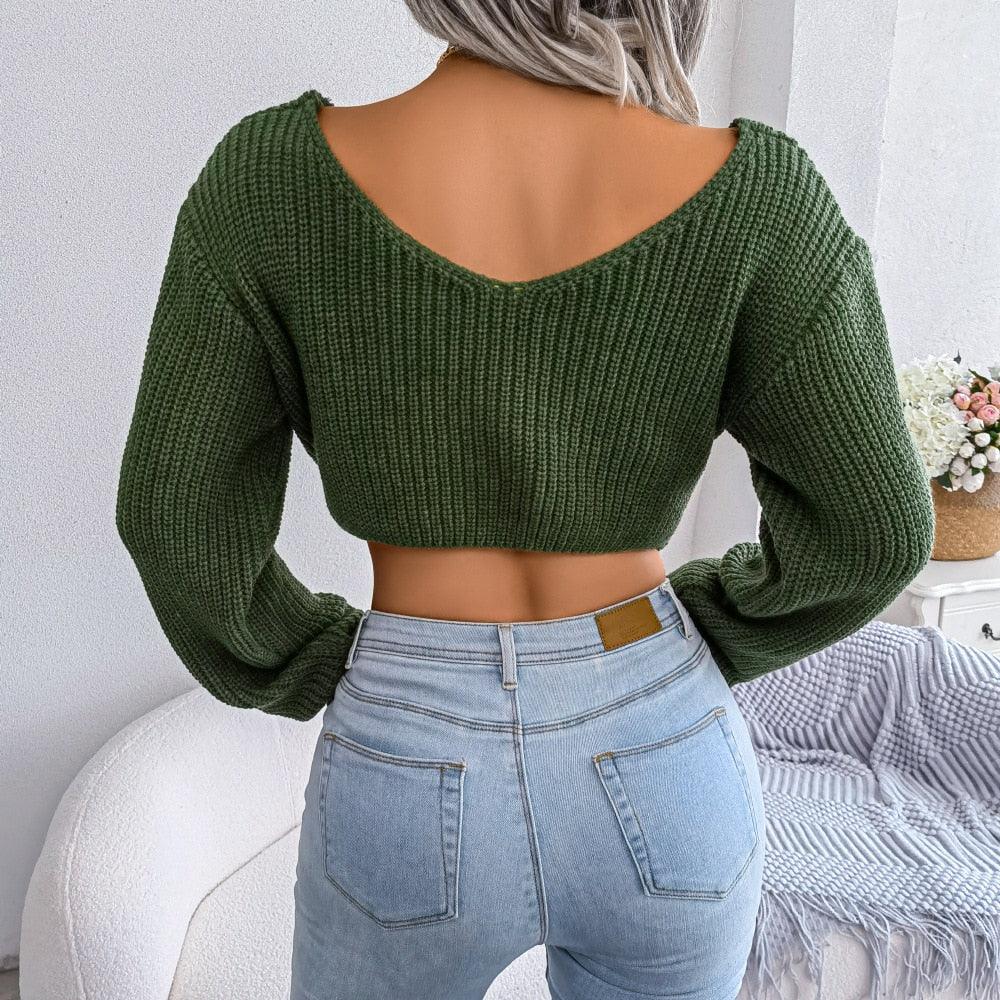 Back view of a woman wearing a green ribbed knit cropped sweater with a V-neckline and light wash jeans.