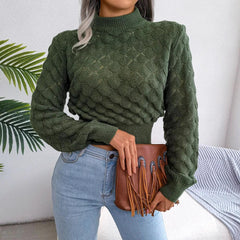 Front view of a woman wearing a green mock neck cropped knit sweater with light wash jeans and a brown fringe clutch bag.