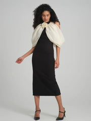 Model wearing a black sheath dress with a white sheer off-the-shoulder overlay and flower accent, posed against a neutral background.