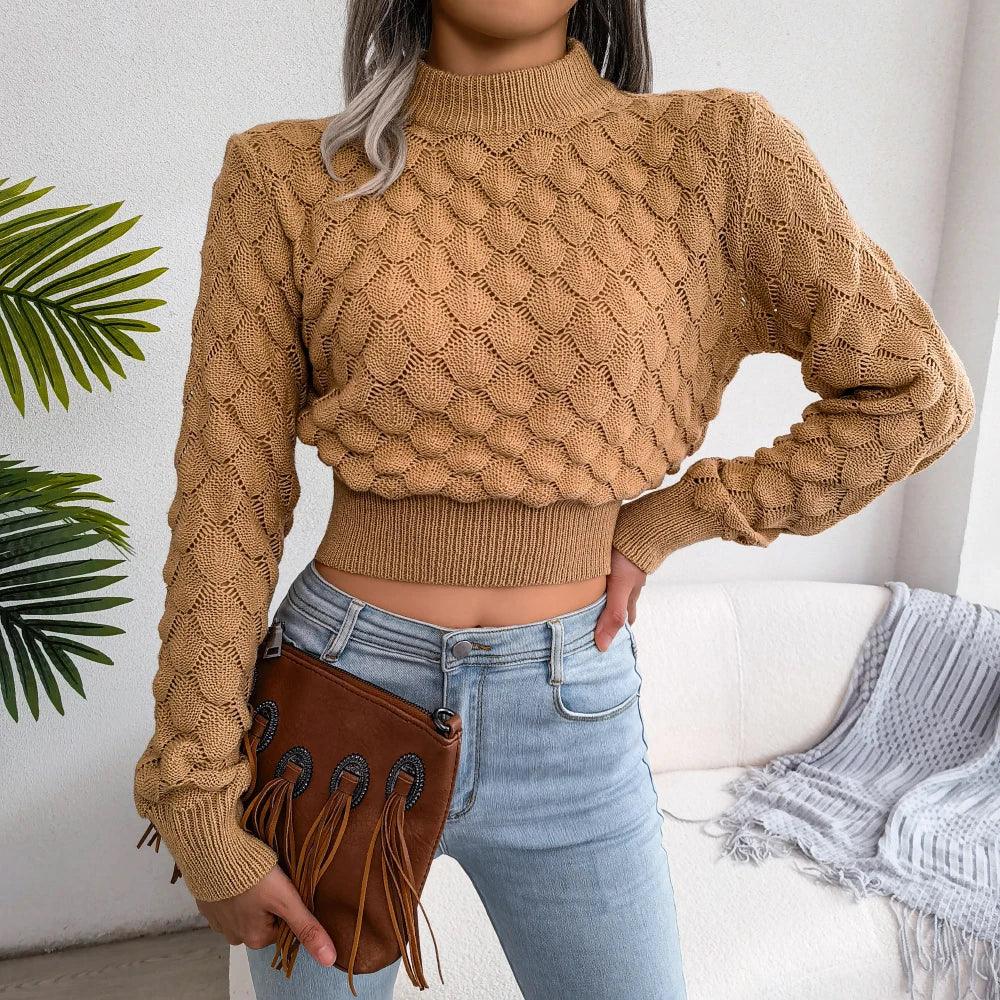 Woman wearing a tan mock neck cropped knit sweater with light wash jeans and a brown fringe clutch bag.