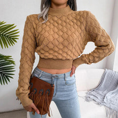 Woman wearing a tan mock neck cropped knit sweater with light wash jeans and a brown fringe clutch bag.