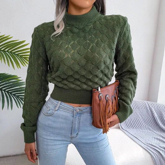 Woman wearing a green mock neck cropped knit sweater with light wash jeans and a brown fringe clutch bag.