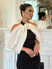 Side profile of a woman in a black sheath dress with a white sheer off-the-shoulder overlay and flower accent, styled with gold earrings.
