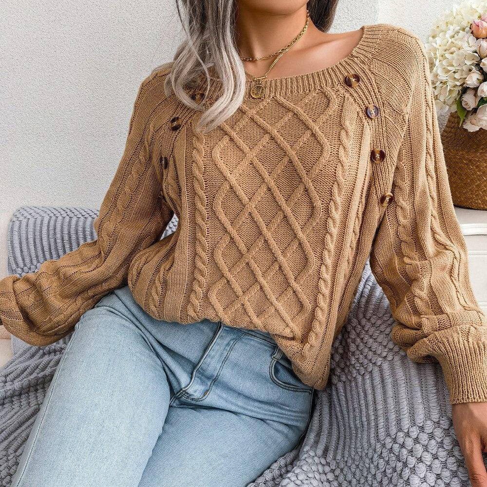 Woman wearing a tan cable knit sweater and blue jeans, sitting on a couch with a grey blanket.