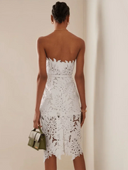 Rear view of a woman in a white strapless lace sheath dress with leaf cutouts and a green handbag.