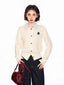 Woman wearing a cream-colored knit cardigan over a striped collared shirt, holding a burgundy handbag.