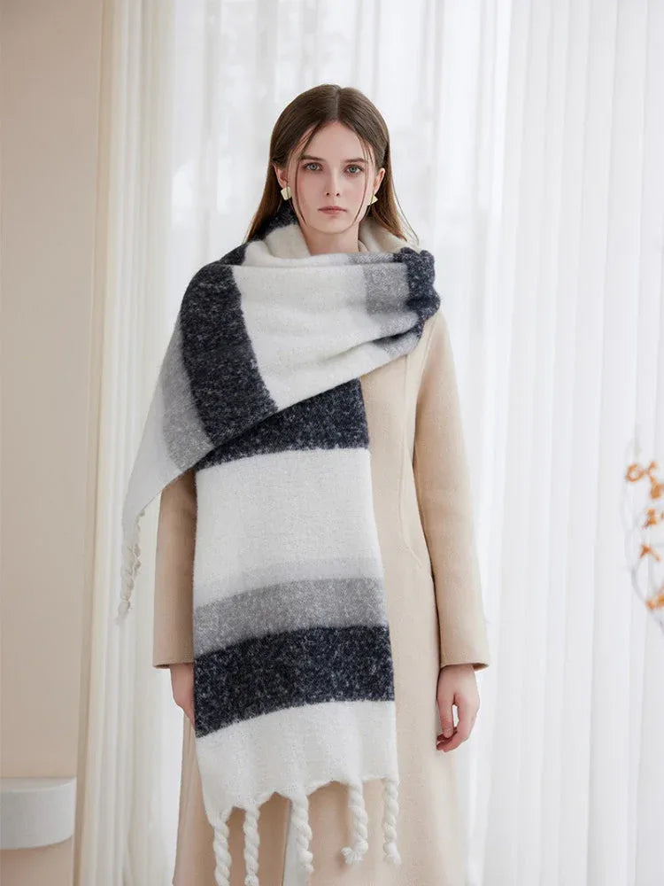Woman wearing a cream coat and a large, striped scarf draped over her shoulders, featuring white, grey, and dark blue bands.