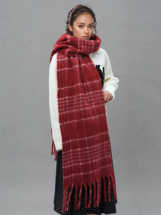 Woman wearing a white sweater with a black graphic and a long red plaid scarf with fringe trim.