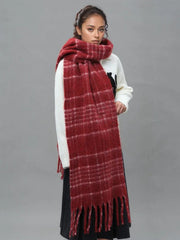 Woman wearing a white sweater with a black graphic and a long red plaid scarf with fringe trim.