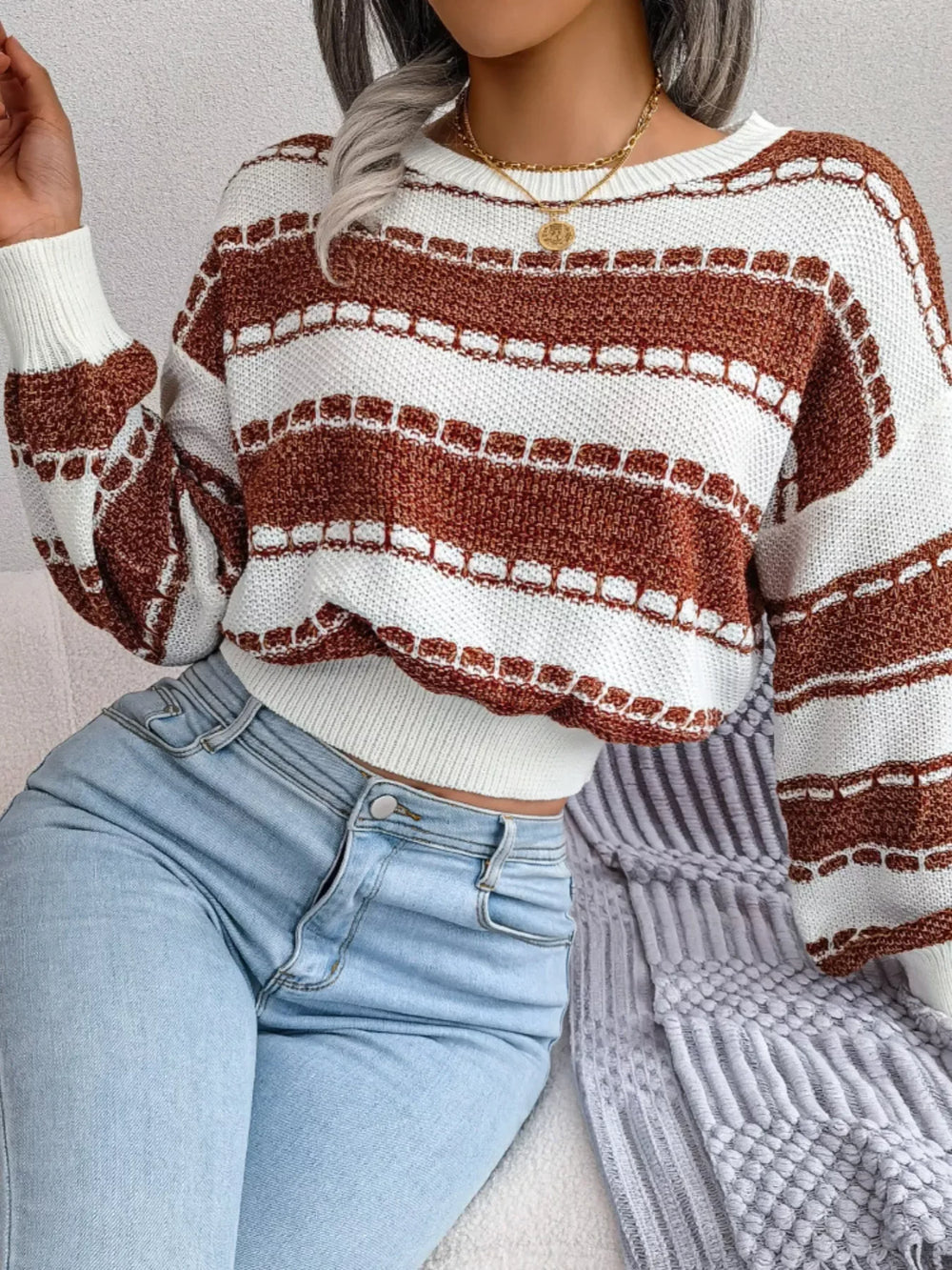 Close-up of a woman wearing a brown and white striped cropped knit sweater and light wash jeans.