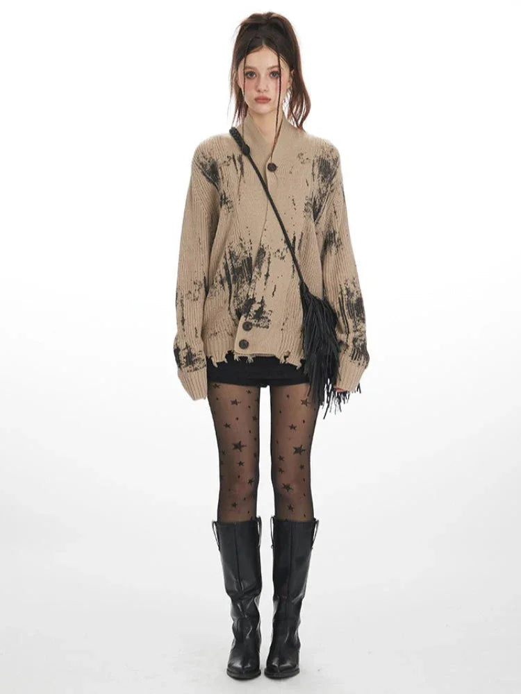 Front view of a model wearing a distressed knit cardigan with a graphic print, paired with black shorts, star-patterned tights, and black boots.