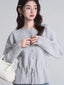 A woman wears a light grey knit cardigan with a drawstring waist and button front closure, paired with blue jeans.