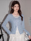 Woman wearing a light blue knit cardigan with white ribbon ties and a white layered skirt.