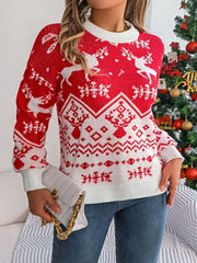 Woman wearing a red and white Christmas sweater with a reindeer pattern and holding a white handbag, standing in front of a Christmas tree.
