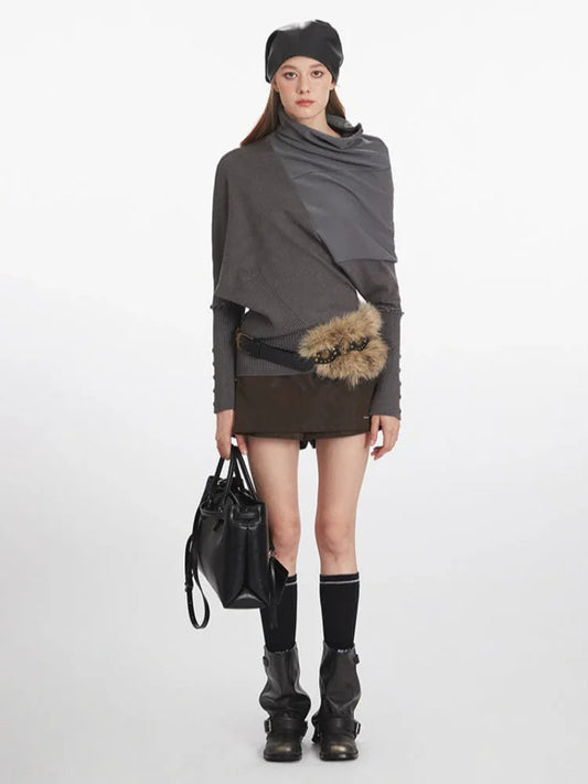 Woman wearing a grey asymmetrical knit sweater with a draped neckline, brown shorts, black socks, black boots, a black leather beret, a black belt with embellishments and a faux fur accent, and holding a black handbag.