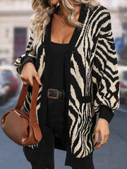 Woman wearing a black and white zebra print longline knit cardigan over a black top and black pants, holding a brown handbag.