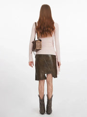 Full-body back view of a woman wearing a pink long-sleeve ruched top, a brown asymmetrical faux leather skirt, patterned tights, and dark boots.