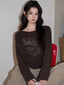 Woman wearing a brown long-sleeved t-shirt with a graphic print, sitting on a red chair.