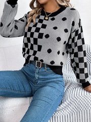 Woman sitting on a couch wearing a gray and black checkerboard and polka dot knit sweater and blue jeans