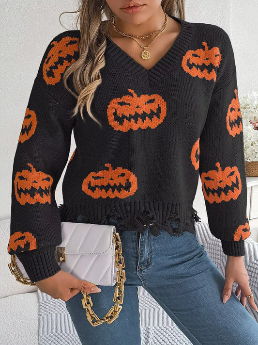 Woman wearing a black long-sleeve v-neck cropped knit sweater with an all-over orange pumpkin print and a distressed hem, paired with blue jeans and a white quilted handbag with a gold chain strap.