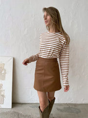 Woman wearing a white and brown striped long-sleeve top, a brown faux leather mini skirt, and brown boots.