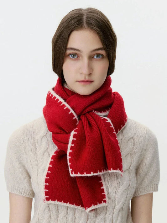 Woman wearing a red knit scarf with white contrast stitching over a cream cable knit sweater, front view.