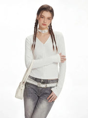 Model posing with a white shoulder bag, wearing a white long-sleeved ribbed V-neck top and grey flared jeans.