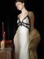 Woman wearing a white satin slip dress with black lace trim, pearl necklace, and faux fur stole.