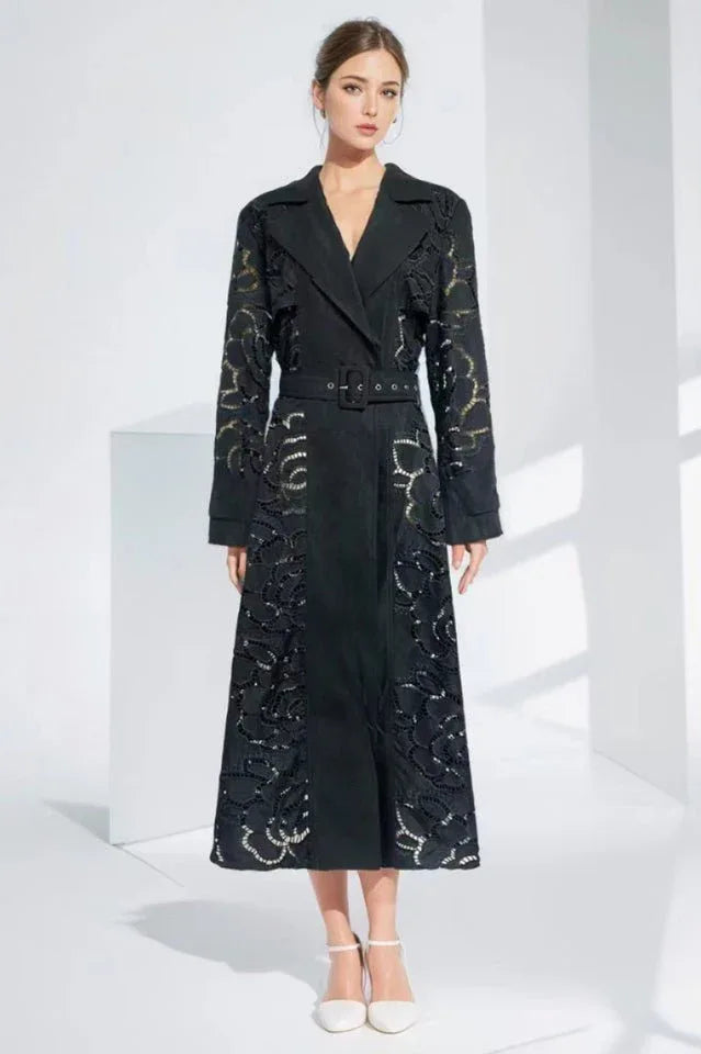 Model wearing a black laser-cut floral trench coat with a belted waist and notched lapels.