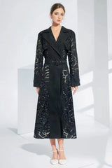 Model wearing a black laser-cut floral trench coat with a belted waist and notched lapels.