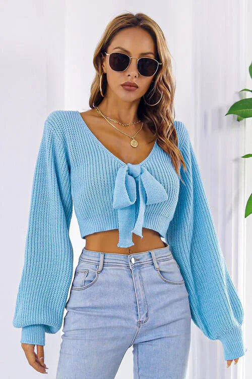 Woman wearing a light blue cropped tie-front sweater with long puffed sleeves and light wash jeans