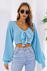Woman wearing a light blue cropped tie-front sweater with long puffed sleeves and light wash jeans