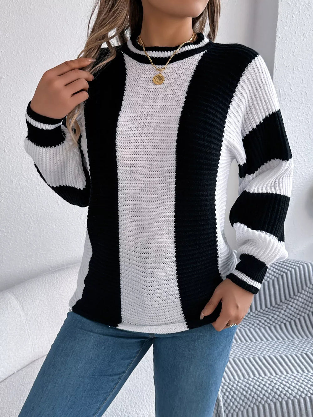 Close-up of a woman wearing a black and white striped knit sweater and blue jeans, touching her hair.