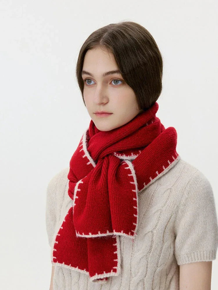 Woman wearing a red knit scarf with white contrast stitching over a cream cable knit sweater, profile view looking left.