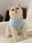 A light blue fuzzy cat sweater with a high neckline and a patch that says "WCAT" is worn by a cream-colored cat looking upwards.
